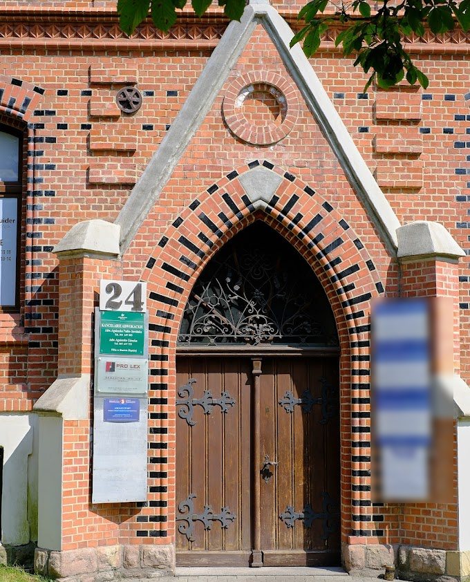 Wejście do kancelarii: portal z czerwonej cegły z czarnymi pasami, ostrołukowe drewniane drzwi z kutymi okuciami